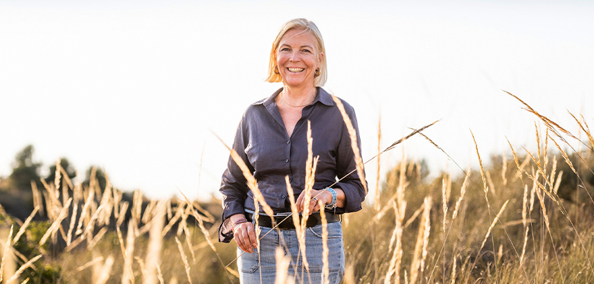 Frau lächelt in einem sonnigen Feld mit hohem Gras.