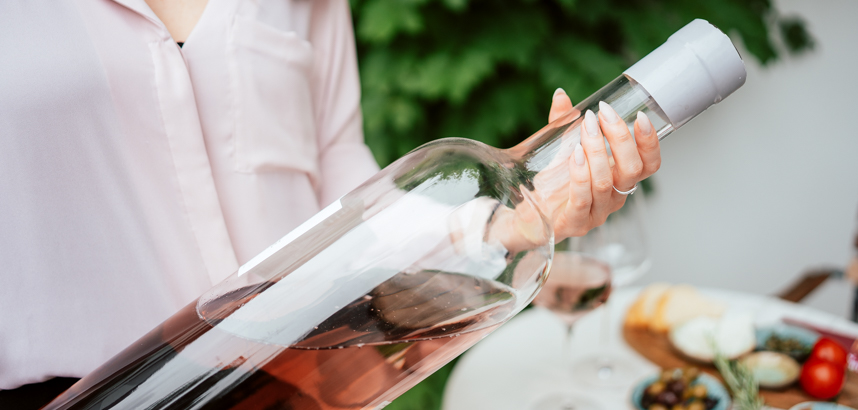 Person hält große Flasche Roséwein, Tisch mit Gläsern und Snacks.