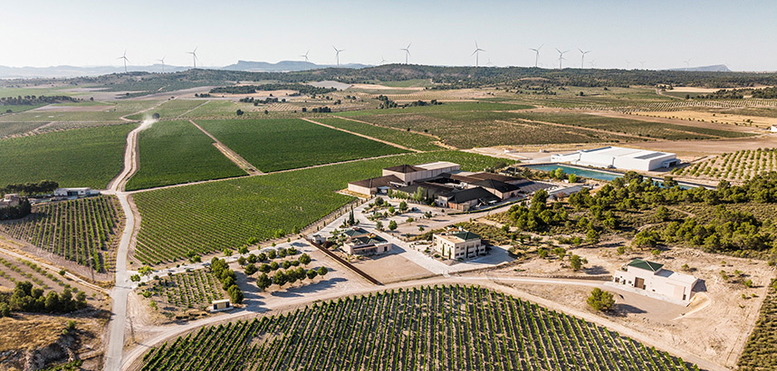 Luftaufnahme einer Weinproduktionsanlage umgeben von Weinbergen und Windrädern.